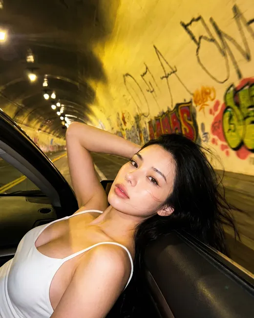 Mei leaning on a car inside a graffiti-covered tunnel